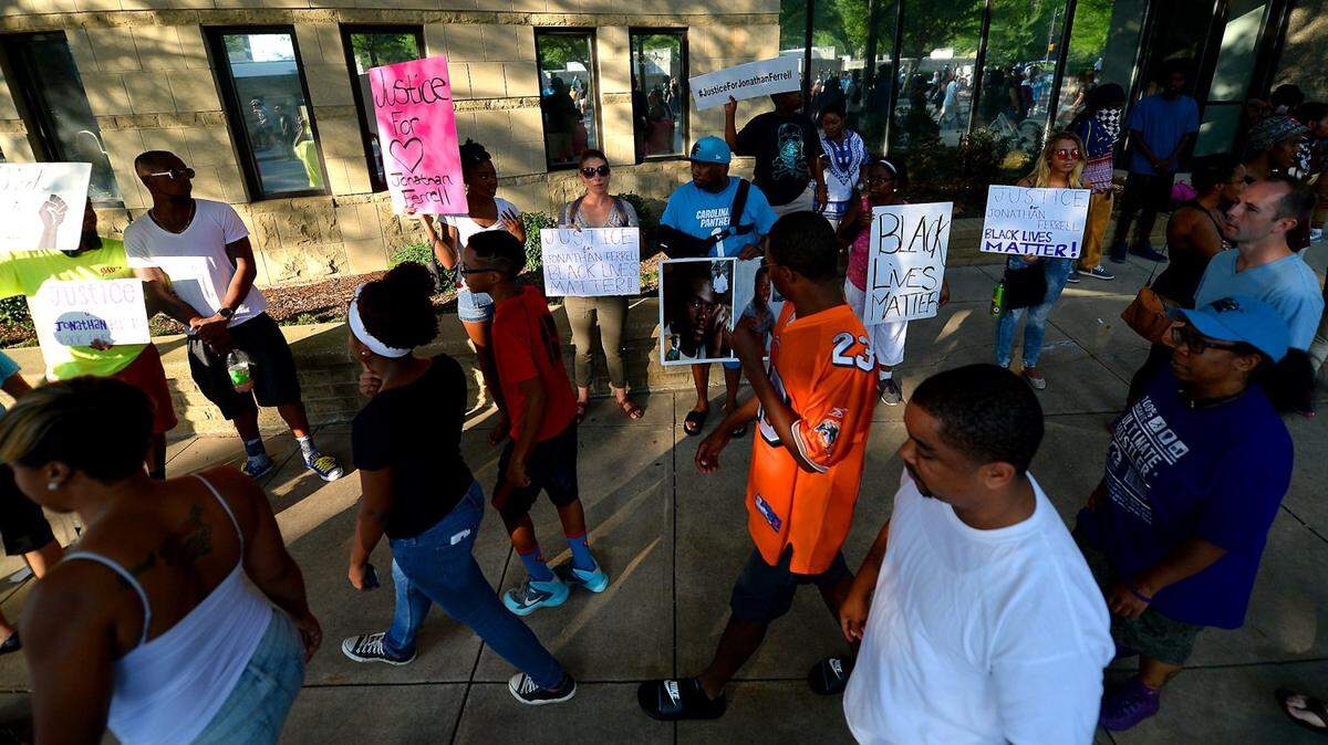 Carolina Panthers and Miami Dolphins fans pass by protesters supporting Jonathan Ferrell on Saturday, August 22, 2015 in Charlotte, NC. Protesters marched on Friday evening and Saturday protesting that after four days of deliberations, a mistrial was declared when the jury was unable to resolve a deadlock in the case of Randall "Wes" Kerrick. Kerrick, a Charlotte-Mecklenburg Police officer accused of killing an unarmed man, Jonathan Ferrell, in a struggle two years ago.