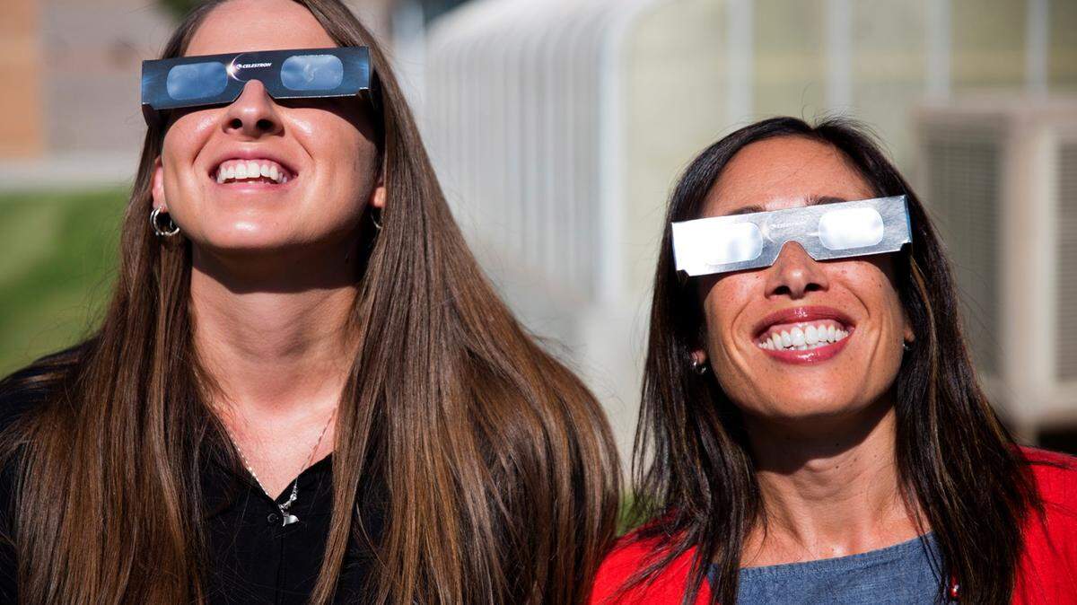 ADVANCE FOR RELEASE SATURDAY, JULY 29, 2017, AT 12:01 A.M. MDT. AND THEREAFTER In this Tuesday, July 18, 2017 photo, Twin Falls High School science teachers Ashley Moretti, left, and Candace Wright, right, use their eclipse shades to look at the sun as they pose for a portrait at Twin Falls High School in Twin Falls, Idaho. The district bought 11,000 pairs of solar glasses, enough for every student and staff member to view the solar eclipse Aug. 21, from Twin Falls.  (Pat Sutphin/The Times-News via AP)