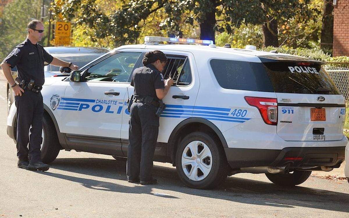 A Charlotte-Mecklenburg police officer talks to  the suspects in the back of the police SUV.Charlotte Mecklenburg law officials secure the scene where a police chase ended at the intersection of Lasalle street and Taylor Avenue. The Wells Fargo bank was robbed this morning on Park road. The suspects where apprehended after their vehicle  crash into another car before the chase ended.