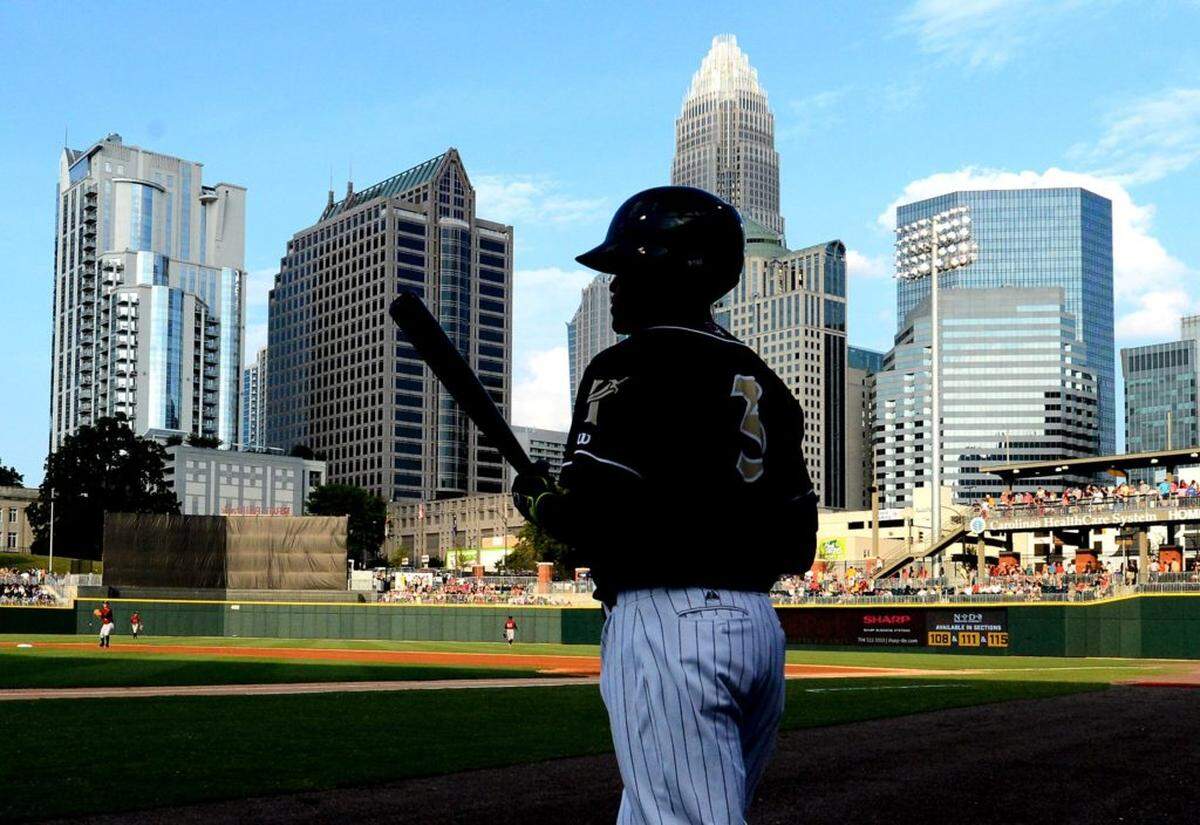 Charlotte Knights Micah Johnson (3) is partially silhouetted against the skyline of Charlotte, NC as he heads to the batters box to face Scranton/Wilkes-Barre Railriders pitcher Bryan Mitchell (15) on Thursday, July 17, 2014 at BB&amp;T BallPark in Charlotte, NC.