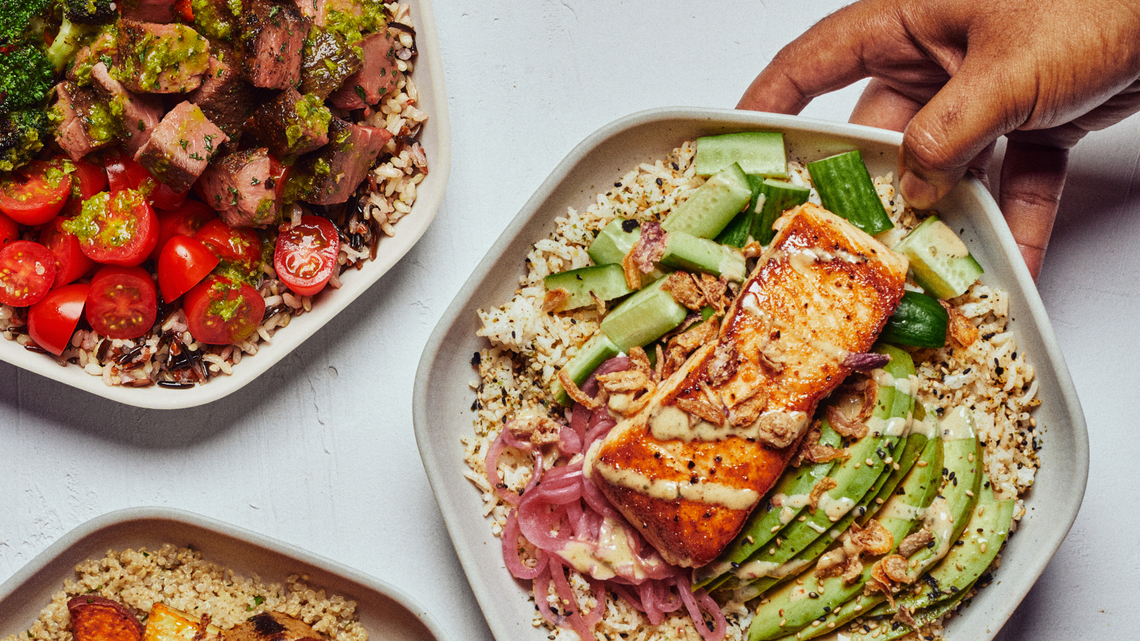 A top-down view shows several healthy protein plates, including one featuring a seared salmon fillet served over rice with sliced avocado and pickled onions. Another plate in the frame features cubed steak topped with chimichurri and paired with bright cherry tomatoes.