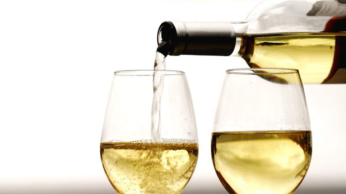 bottle of white wine being poured and two glasses