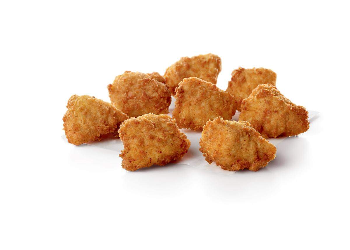 Eight golden-brown Chick-fil-A Nuggets are piled loosely on a small white piece of paper against a plain white background. The boneless chicken pieces are fried and have a textured, crispy coating.