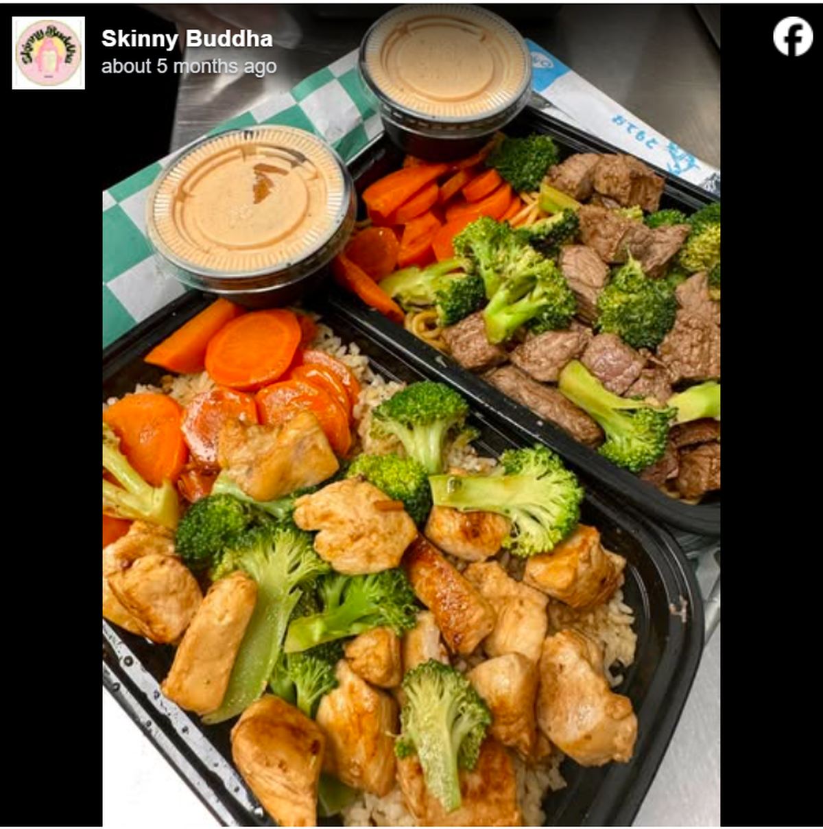 A top-down view of two takeout containers from Skinny Buddha, one filled with grilled chicken and the other with steak, both served alongside steamed broccoli and carrots. Each meal includes a side of creamy orange dipping sauce and is presented on a green and white checkered surface.