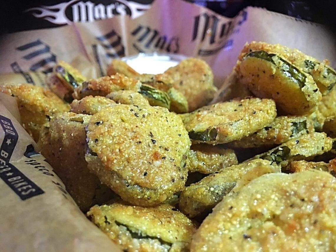 Close-up of a basket of crispy, deep-fried pickle slices, lightly dusted with spices, served with a small cup of dipping sauce in the background.