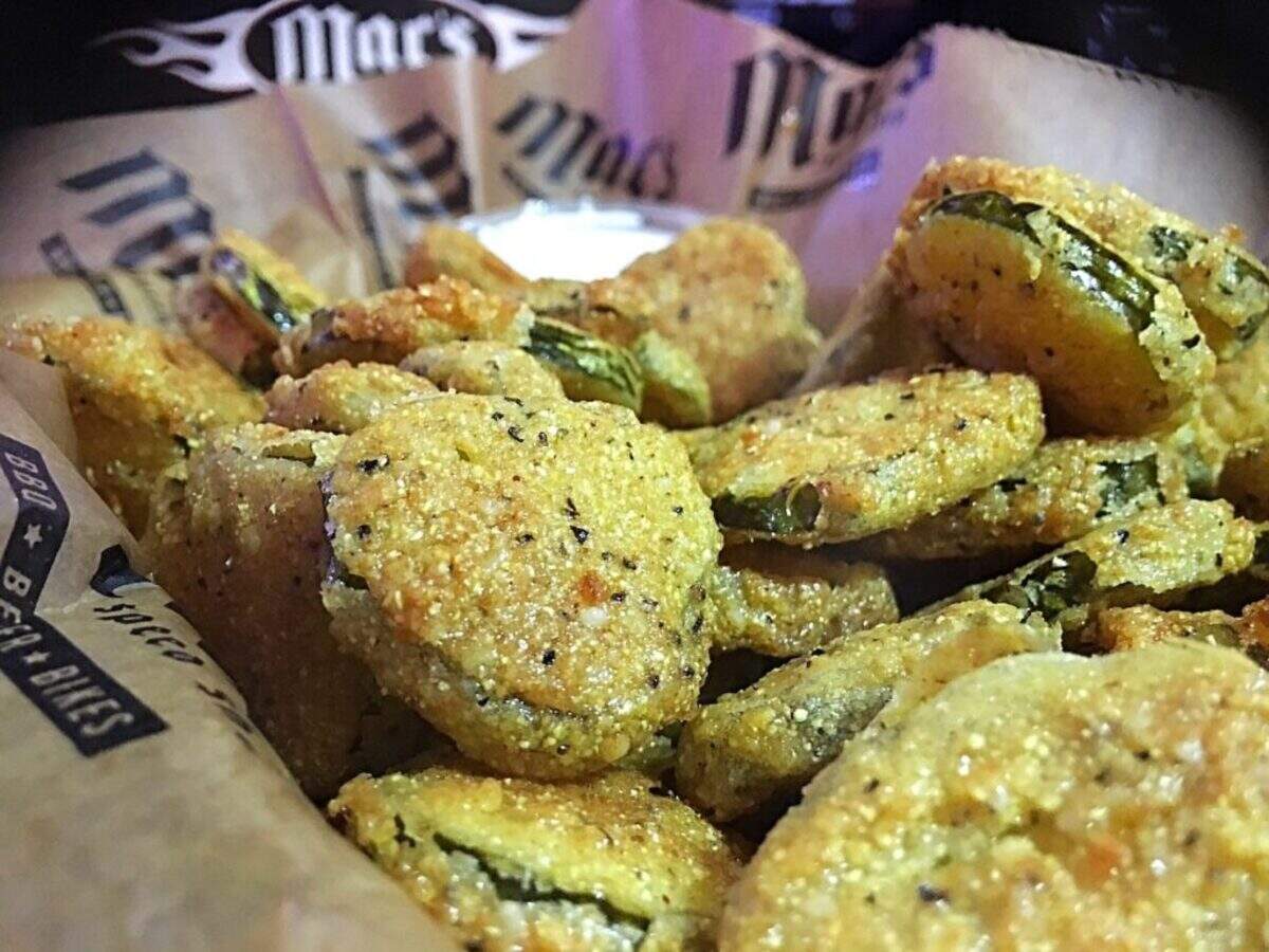 Close-up of a basket of crispy, deep-fried pickle slices, lightly dusted with spices, served with a small cup of dipping sauce in the background.