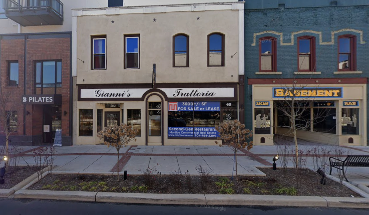 A street-level view of a sidewalk featuring storefronts for a Pilates studio, Gianni’s Trattoria, and an arcade bar called Basement. The Gianni’s Trattoria windows display a blue “For Sale or Lease” sign from Mortice Commercial Real Estate.