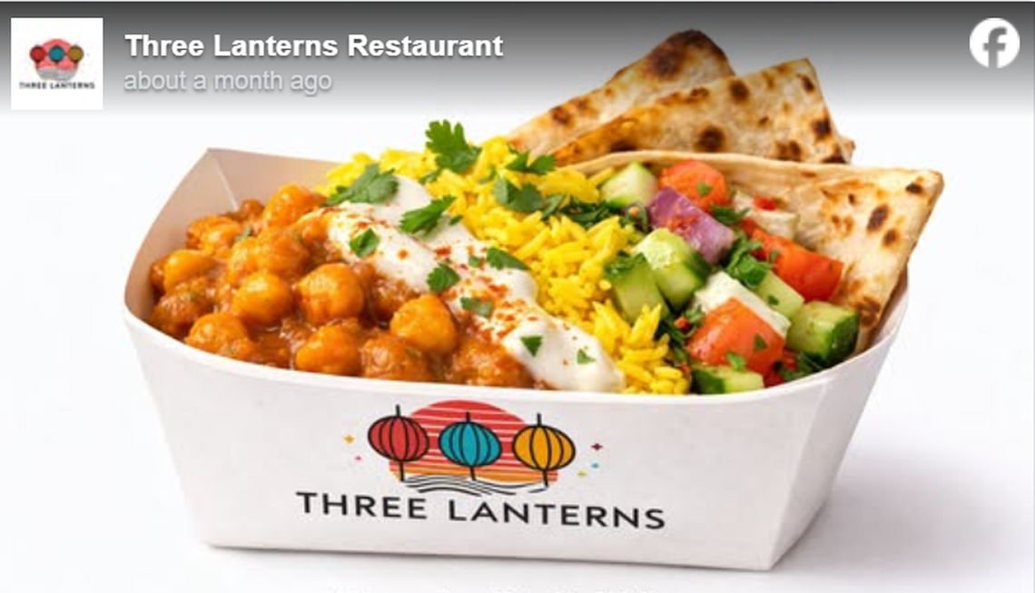 A white paper food container with the “Three Lanterns” logo is filled with a colorful meal of chickpea curry, yellow basmati rice, and a fresh cucumber and tomato salad. The dish is topped with a dollop of white sauce and fresh cilantro, served with two pieces of toasted flatbread on the side. The image is a social media post from Three Lanterns Restaurant, featuring their branding on both the box and the profile icon.