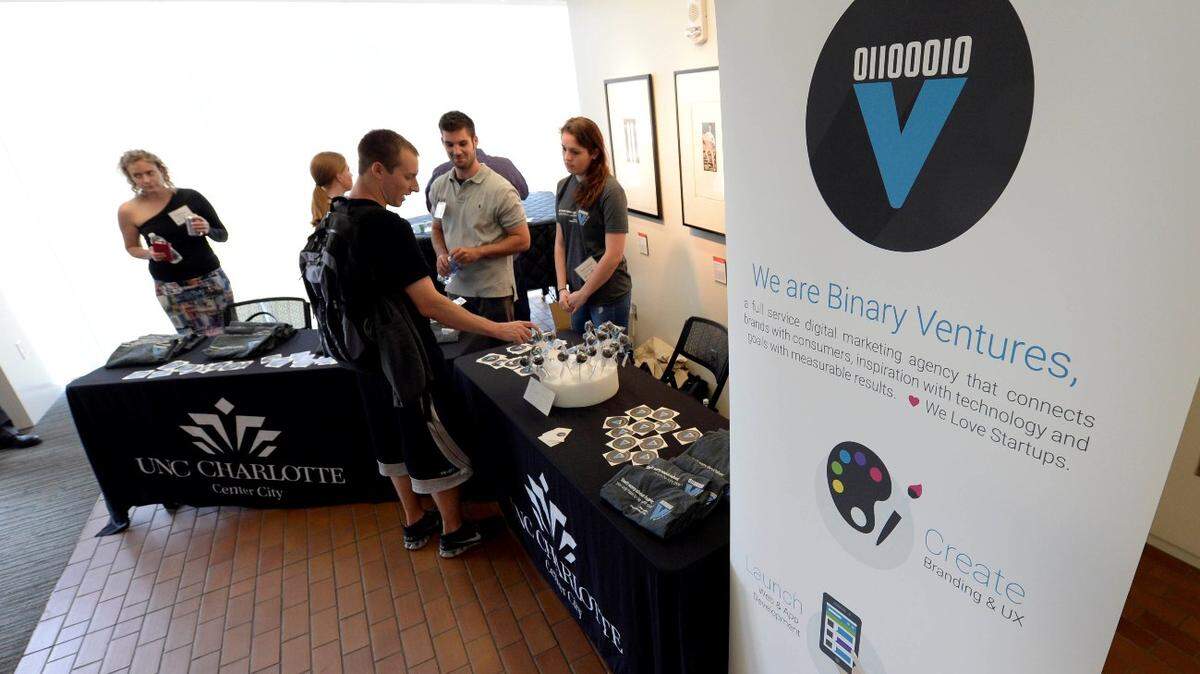 People mingle around the Binary Ventures table, a program supporter of RevTech Labs, prior to the start of presentations as part of Demo Day for entrepreneurs who are members of the fourth class of RevTech Labs, Packard Place's 12-week startup incubator and accelerator program. at UNC Center City. UNC Charlotte Center City on Wednesday, May 20, 2015.