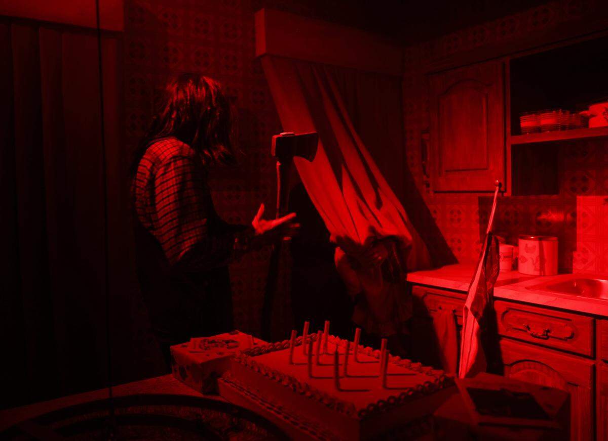 An ax-wielding man scares a person behind a curtain Tuesday, Sept. 9, 2025 at The Conjuring: Beyond Fear experience at Scarowinds.