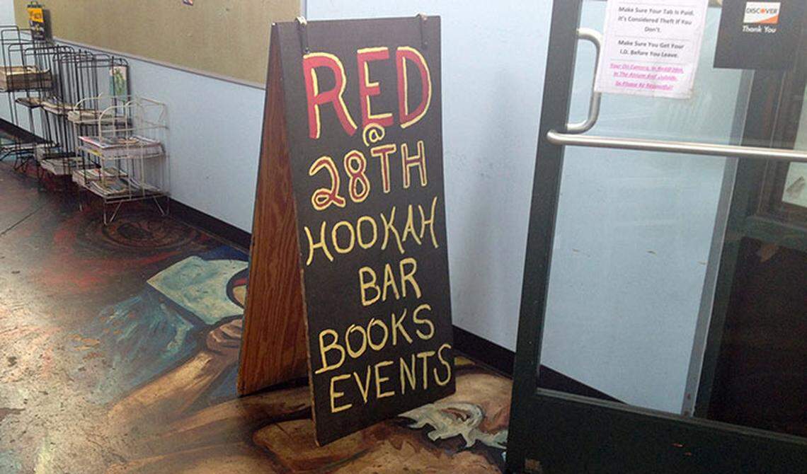 A dark wooden A-frame sign stands in a hallway, featuring “RED @ 28TH” written in red and yellow chalk. Below the name, the sign lists the venue’s offerings: Hookah Bar, Books, and Events.