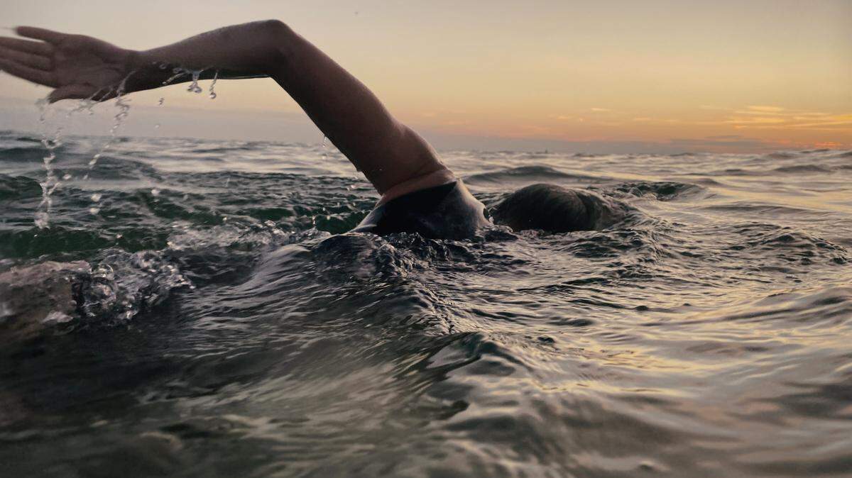 A person swims in the ocean at sunset.