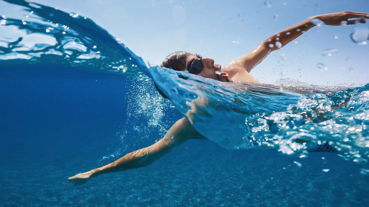 A man exercises by swimming in the ocean with a swim cap and goggles on.
