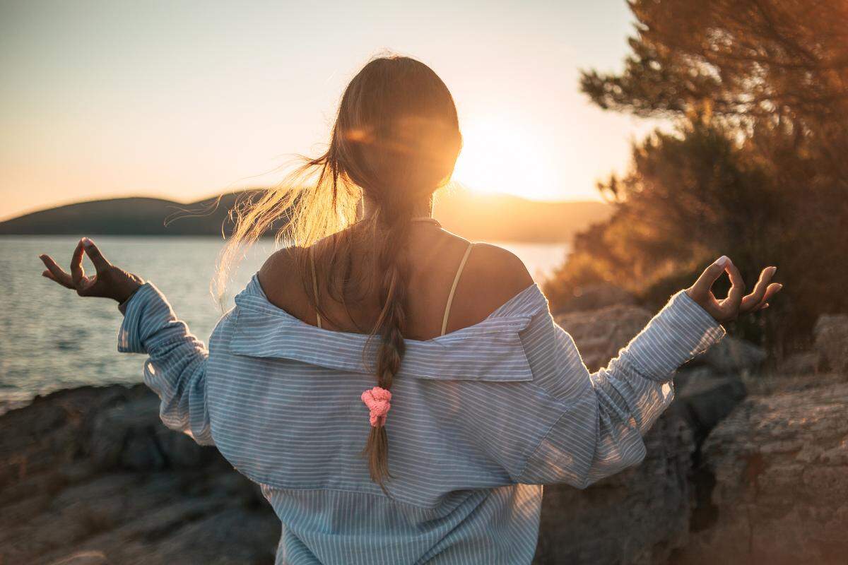 One woman, a young woman on a reef by the sea, meditates at sunset in the evening, watching the sun set over the sea.