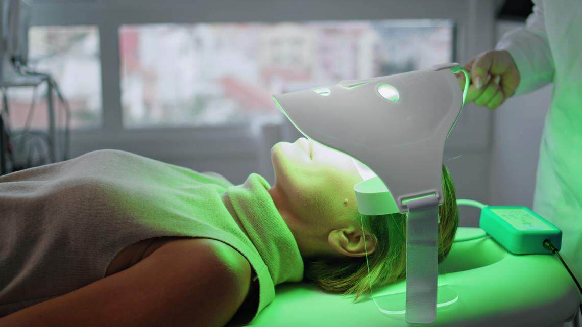 A woman receives green light therapy on her face. Devices using light and sound waves are gaining in popularity to combat the effects of skin aging.