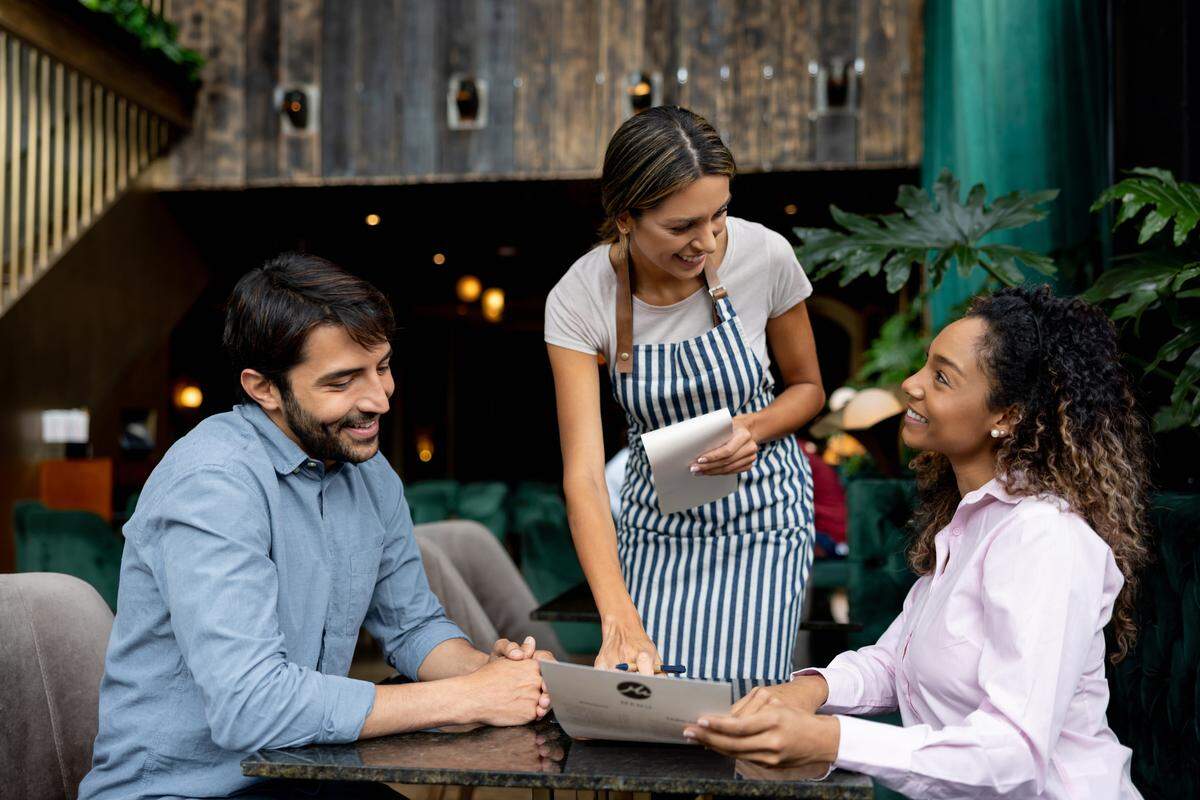 Couple of clients eating at a restaurant asking questions about the menu to the waitress.