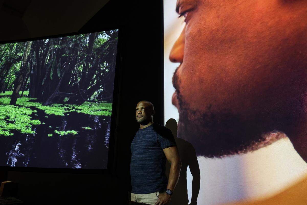Davian Robinson, who is visually impaired, stands between two video screens at the Bechtler’s new exhibit that he collaborated on.