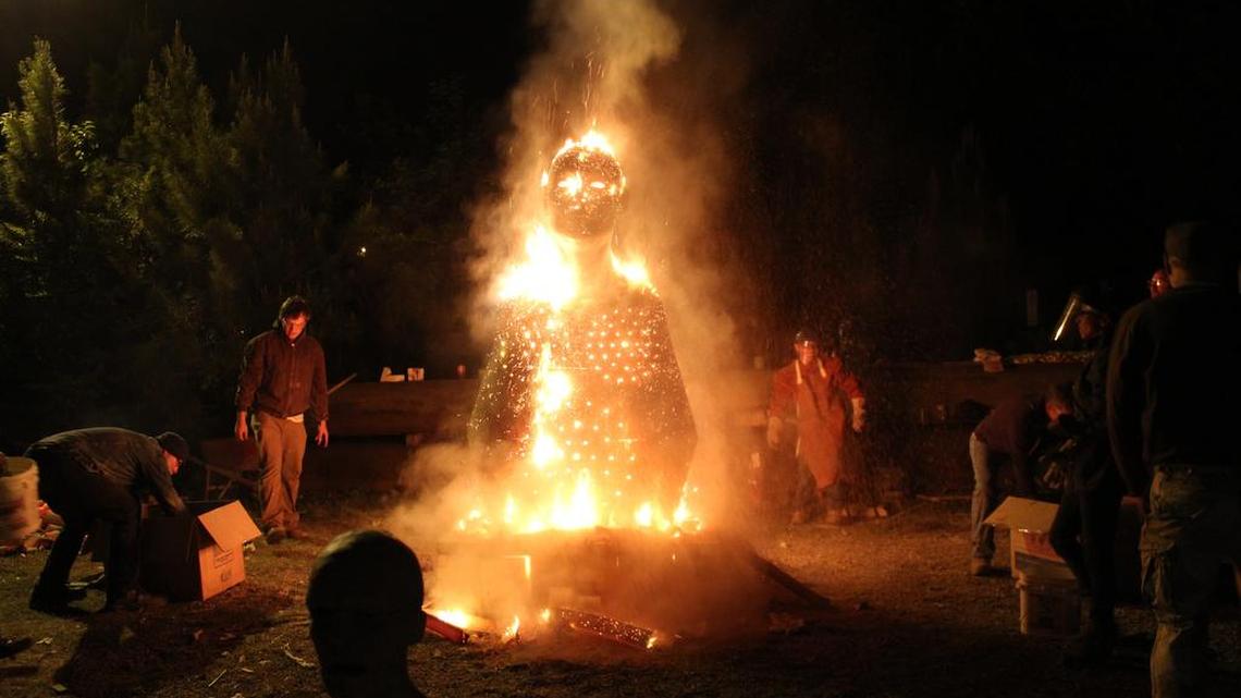 Glaze materials are thrown onto the 2014 FireFest sculpture, “Fireman” by Cristina Cordova, of Penland.