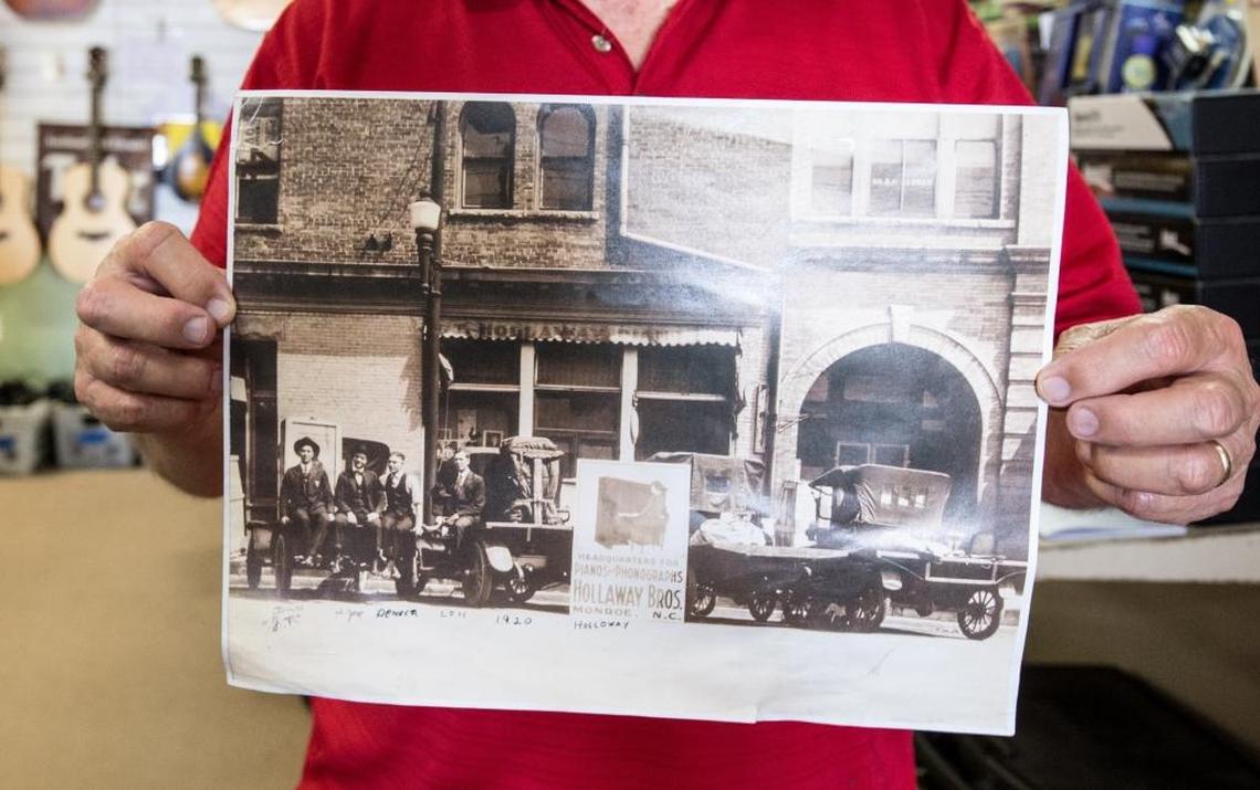 Marion Holloway holds up the earliest photo of his grandfather, J.T. (that’s him on the left), in front of the store, in 1920.