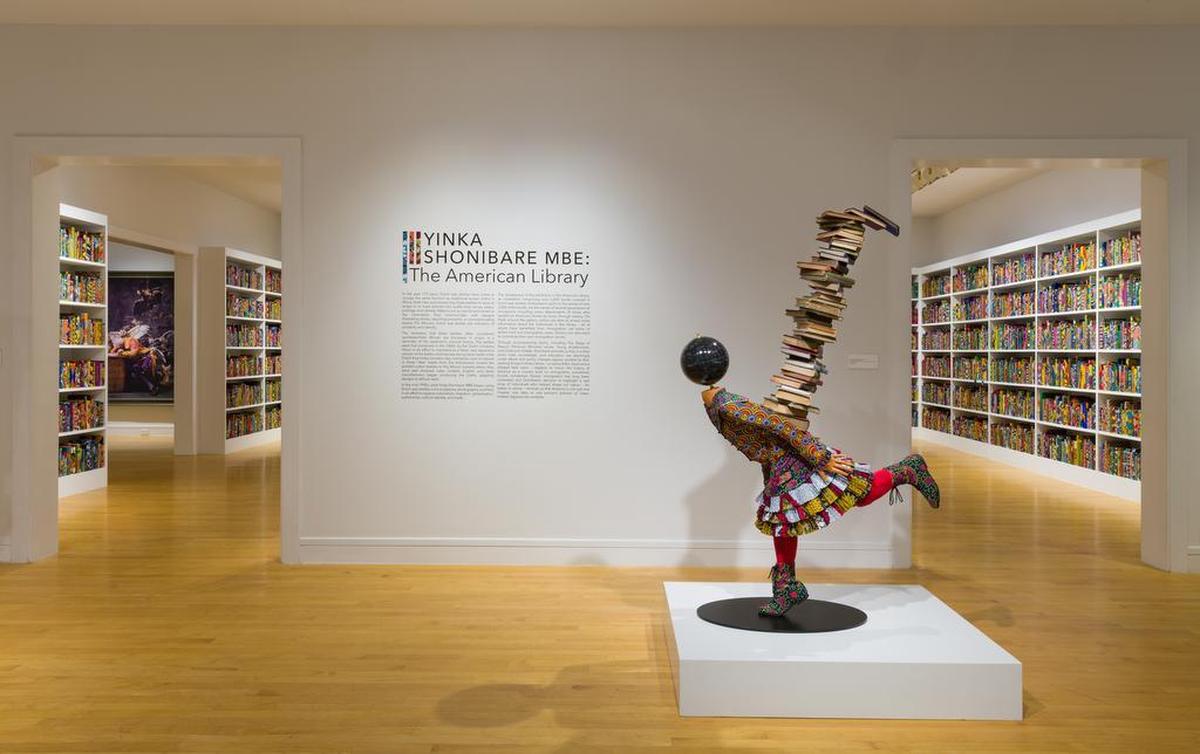 An installation view of “The American Library” by Yinka Shonibare MBE at Davidson’s Van Every/Smith Galleries. (That MBE denotes Most Excellent Order of the British Empire, an honor from the Queen.) Hardback books, Dutch wax printed cotton textile, gold foiled names, interactive application.