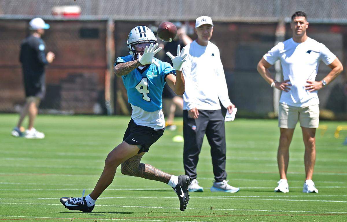 Carolina Panthers rookie wide receiver Tetairoa McMillan, left, keeps his eyes on the ball as he catches a pass during the team’s rookie minicamp practice on Friday, May 9, 2025. At right, head coach Dave Canales watches.