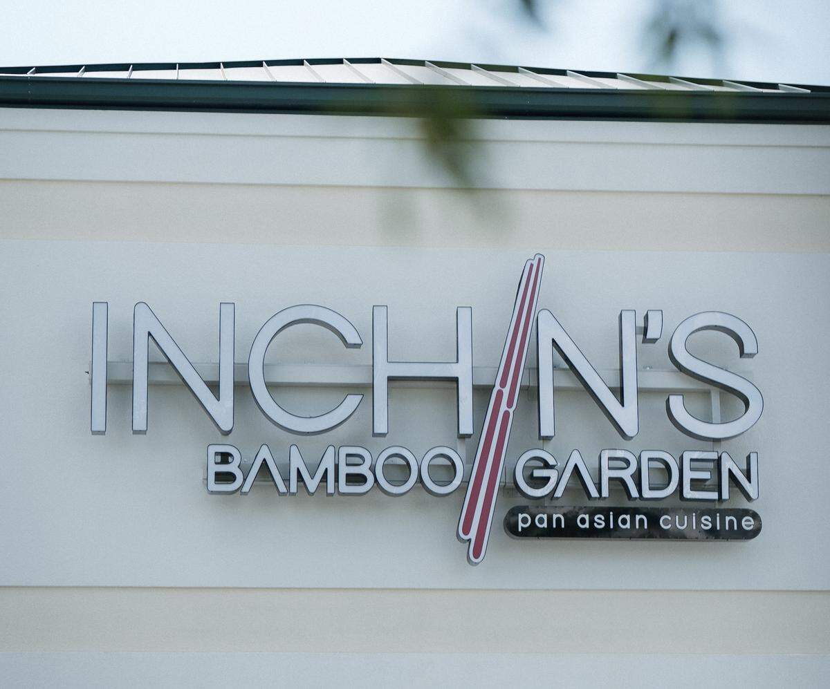 A closeup of the exterior sign for “Inch’n’s Bamboo Garden.” The sign features silver letters with a red diagonal line and the words “pan asian cuisine” in smaller text below.