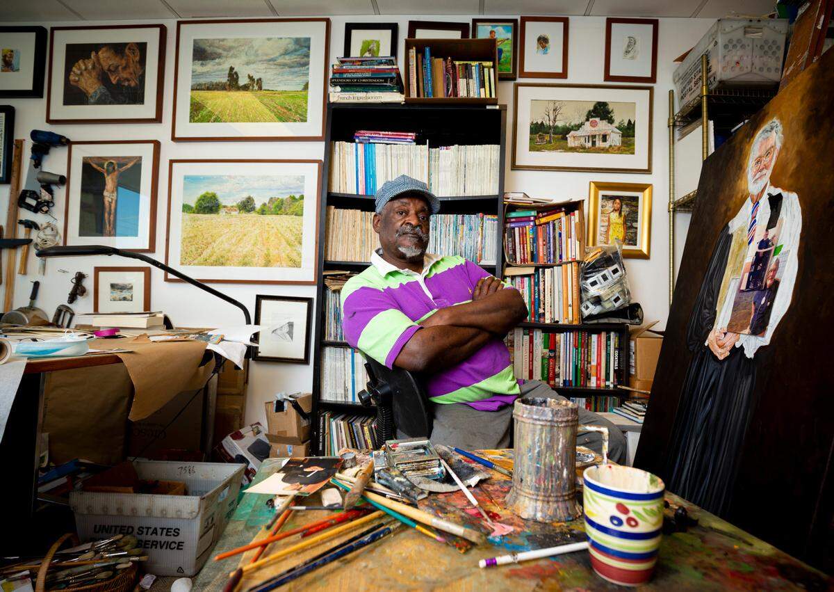 Artist Tommie Robinson poses for a portrait in his Charlotte studio. Robinson started drawing at age 7 after his father died as a way to process his thoughts. He’s been painting full-time for decades and two of his most well-known works, the 24-foot-tall “Banking and Commerce” and “Transportation” murals, hang at the Spectrum Center uptown. 