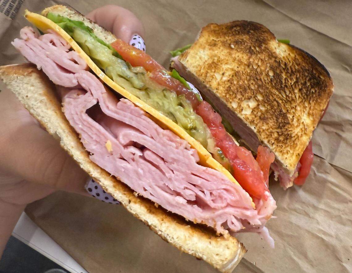 The sandwich filling is clearly visible and includes what looks like a generous amount of sliced ham, a slice of cheese, fresh tomato slices, and pickles. The bread is toasted and has a nice golden-brown color.