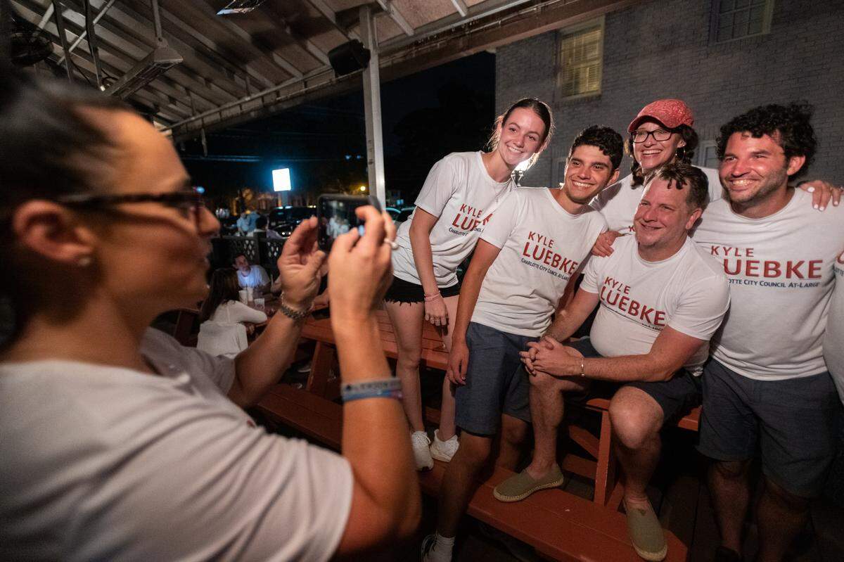 Kyle Luebke (right), a Republican candidate for City Council At-Large, poses for photos with his campaign team at Selwyn Avenue Pub as ballots are counted in Charlotte, N.C. on Tuesday evening, July 26, 2022. Among Luebke’s campaign team are his mother (third right), and fiancé (second right). Luebke trailed behind the fourth-place at-large seat, James “Smuggie” Mitchell by more than 10,000 ballots.