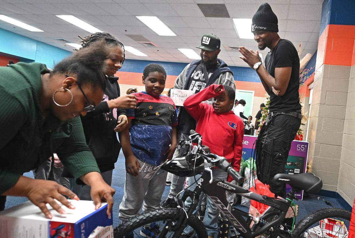 Charlotte Hornets forward Brandon Miller, right, rubs his hands together as Brianna Downs, left, unwraps a Christmas present for her children Emmerson, Carter and Braxton at the Boys and Girls Club of Cabarrus in Concord, NC on Tuesday, Dec. 16, 2025. Miller and his foundation surprised families with gifts ahead of the Christmas holiday.