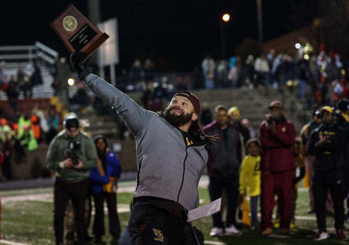 West Charlotte head coach Sam Greiner runs with the trophy after his team won the NCHSAA 3A regional championship, defeating Hickory 36-20, at Hickory High School on Friday, December 13, 2024.