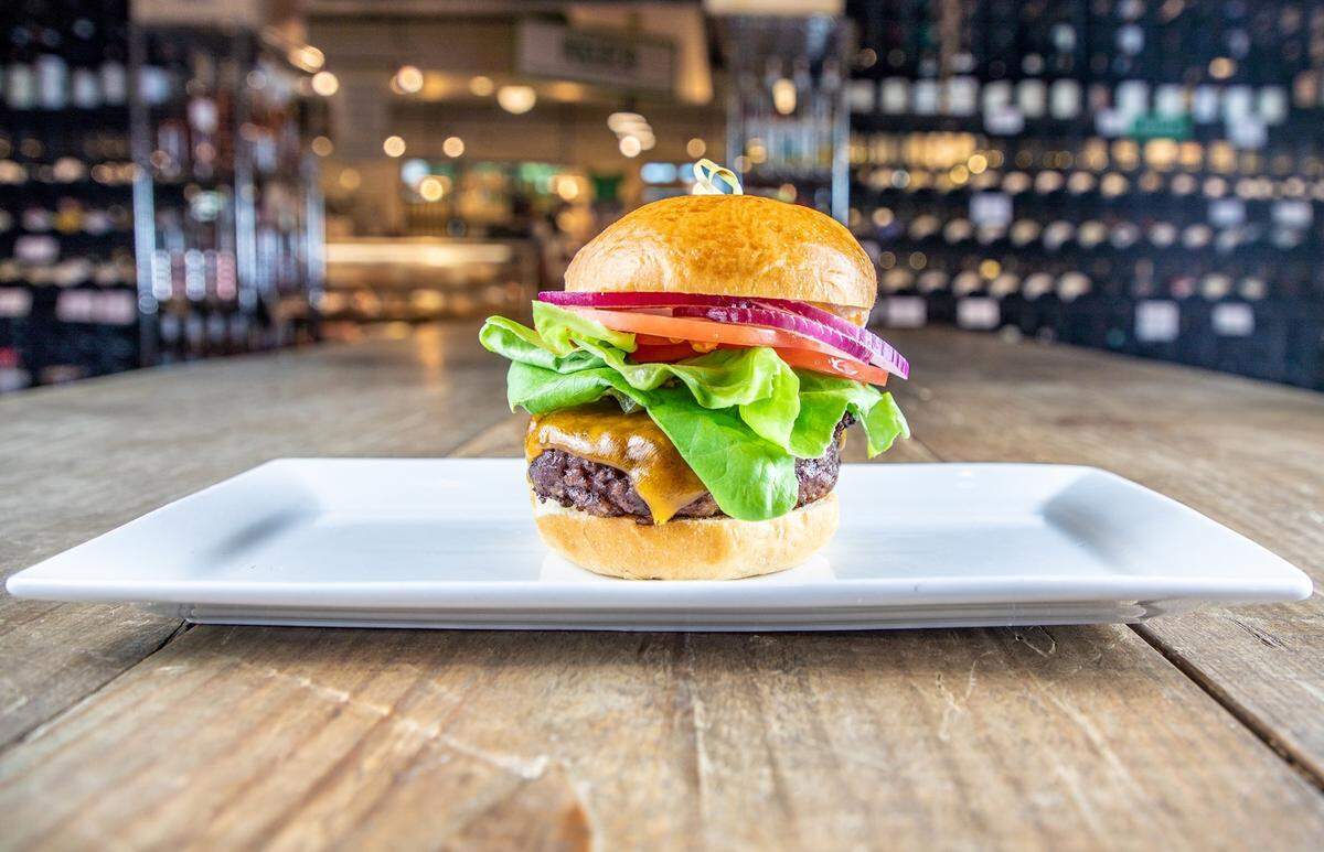 A thick steakburger with melted cheddar cheese, fresh bibb lettuce, tomato, and red onion on a brioche bun, centered on a white rectangular plate.