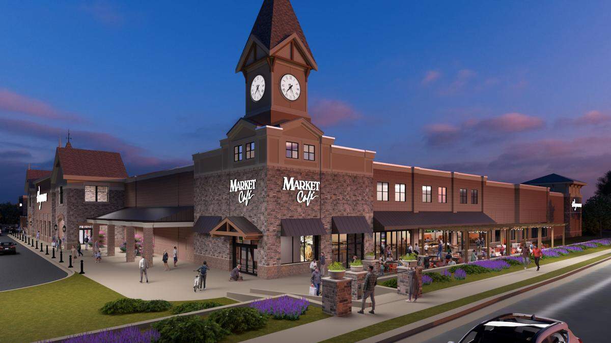 An aspirational architectural rendering of the “Market Cafe” at dusk. The large building features a prominent clock tower over the main entrance. To the right, a long covered patio is filled with people eating at tables. The building is surrounded by sidewalks and landscaping with purple flowers.