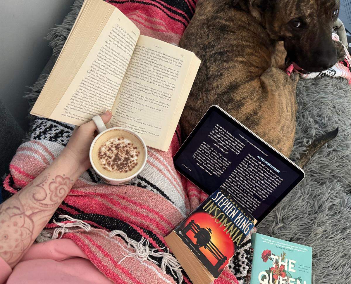 A pile of books rests alongside Charlie the dog, including the e-book version of “Inflamed: Deep Medicine and the Anatomy of Injustice” by Raj Patel and Rupa Marya.