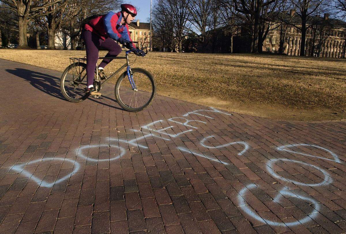A bicyclist pedals by the message “Doherty is God” that was spray-painted on a sidewalk on the UNC campus after the Tar Heels upset Duke early in the 2001 season.