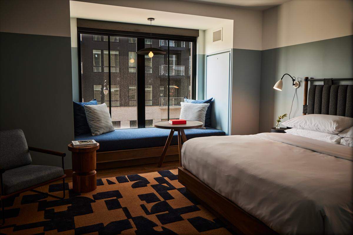 The Junto’s Executive King Suite blends industrial chic with comfort, featuring a window seat overlooking tree-lined parks.
