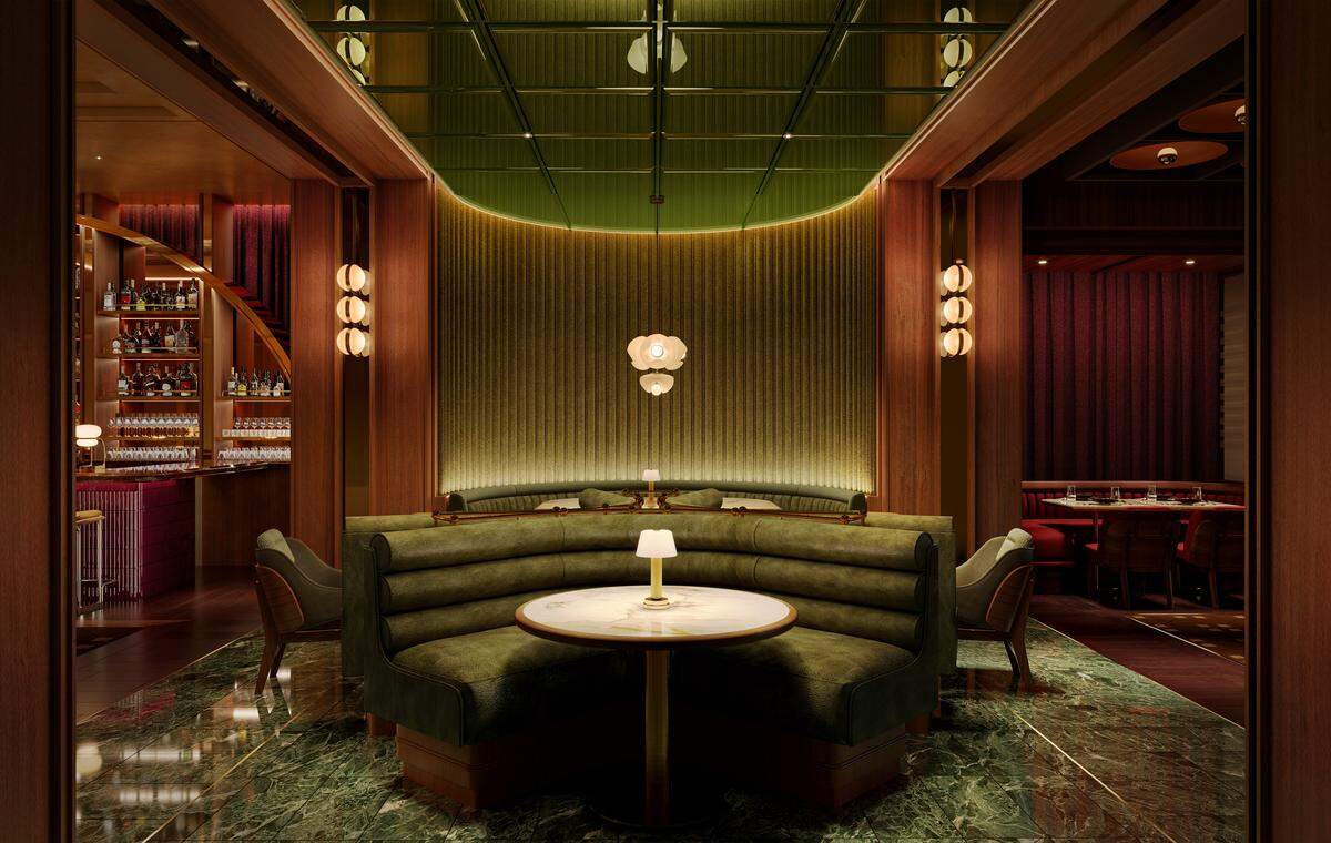 An architectural rendering looking into a luxurious steakhouse entrance. In the center, a semi-circular booth wrapped in olive-green velvet faces a round white-and-gold marble table illuminated by a small brass cordless lamp. The floor features highly polished green marble tiles with strong white veining. The background wall is finished with vertical, undulating gold metallic slats beneath a glossy green tiled ceiling grid. To the left, a warmly lit bar with glass shelving and stacked bottles is visible through rich wood pillars.
