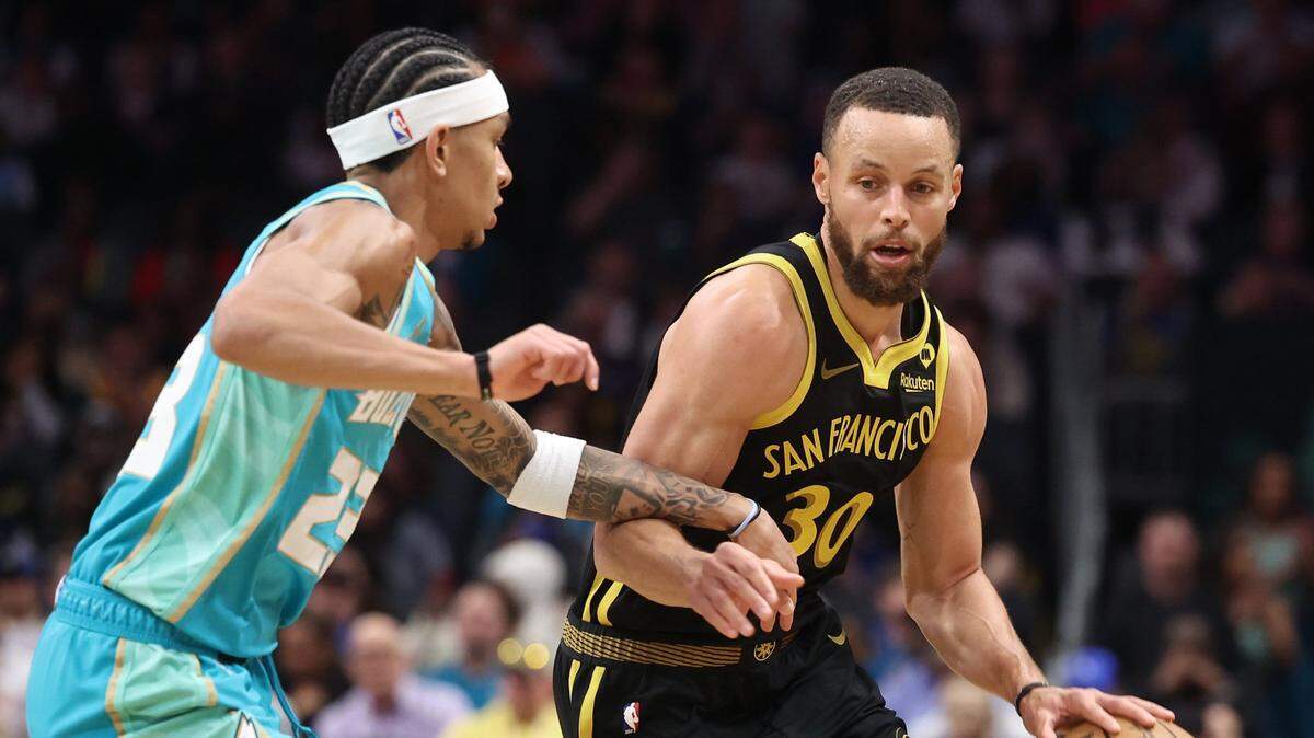 Golden State Warriors guard Steph Curry, right, begins to drive around Charlotte Hornets guard Tre Mann, left, during first quarter action at Spectrum Center in Charlotte, NC on Friday, March 29, 2024.