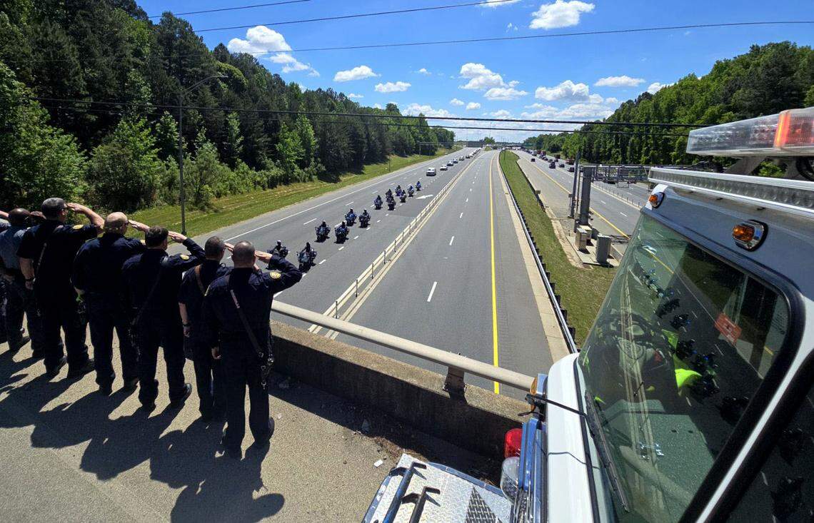 Firefighters and sheriff deputies on the Cindy Lane Bridge salute a processional on I-77 for Deputy U.S. Marshal Thomas “Tommy” Weeks Jr. Weeks, of Mooresville, was one of four officers fatally shot while serving a warrant in east Charlotte on April 29.