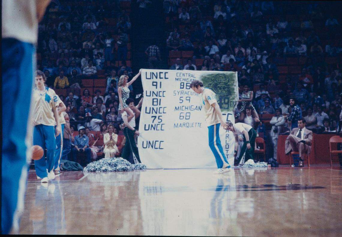 Charlotte 49ers cheerleaders show off a banner before the NCAA Final Four in 1977. The banner details the final scores of Charlotte’s previous NCAA tournament wins that year, including an upset victory over No. 1 Michigan.