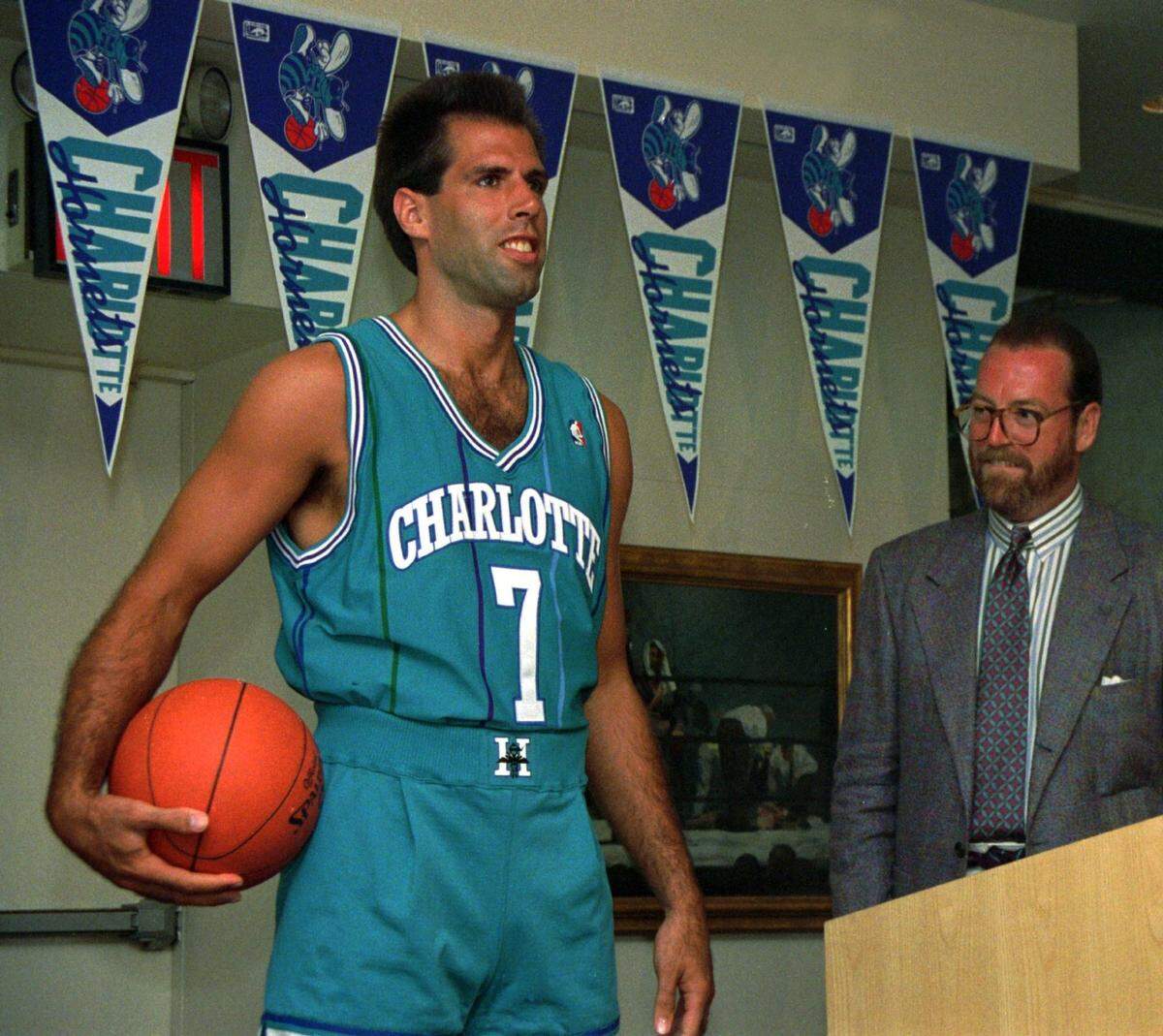 Former Charlotte Hornets forward Kelly Tripucka models Alexander Julian’s new uniform in 1988. The cursive font on the pennant in the background inspired the script across the chest of the Hornets’ 2021-22 City Edition uniforms.