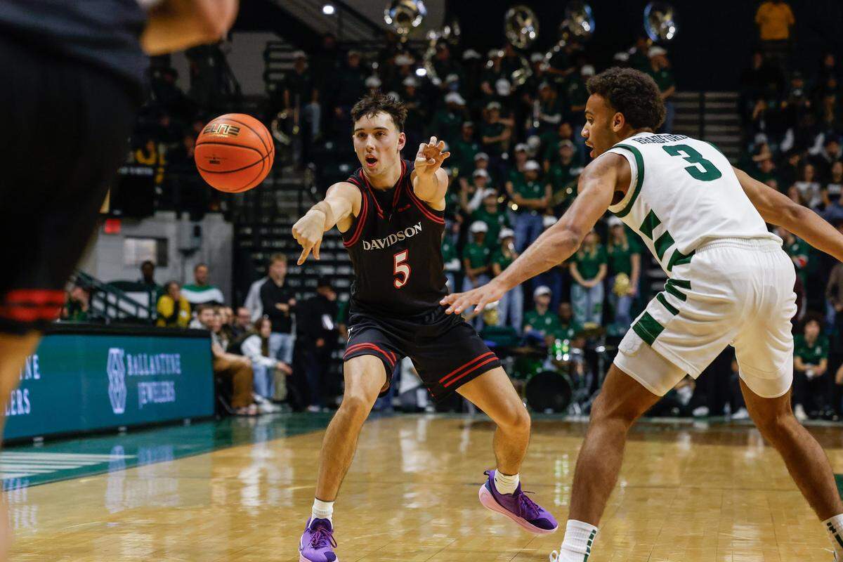 Davidson guard Parker Friedrichsen passes to a teammate as Charlotte guard Ben Bradford defends during the game at Dale F. Halton Arena in Charlotte, NC on Tuesday, November 11, 2025.