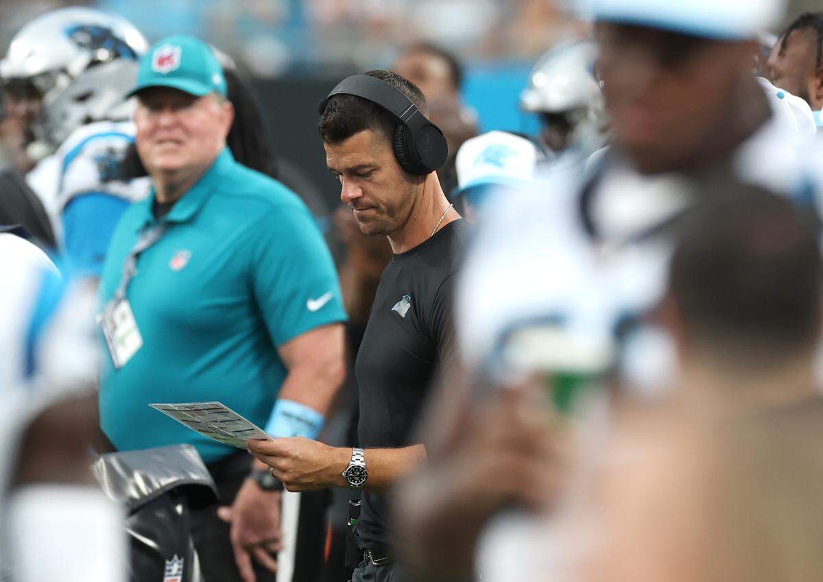 Carolina Panthers head coach Dave Canales, center, looks over his call sheet during the preseason. Canales plans to take a similar sheet to the top of the Superdome before Sunday’s game, looking down at the field and visualizing what play he will call in certain “difficult” situations.