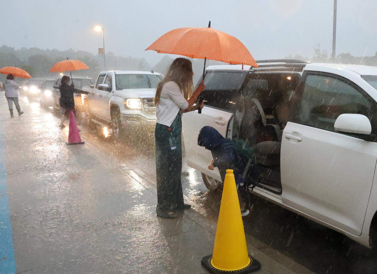 School staff at Fort Mill’s River Trail Elementary School try to stay dry as they help kids out of cars on the first day of school. The district held school despite hurricane Debby soaking the area.