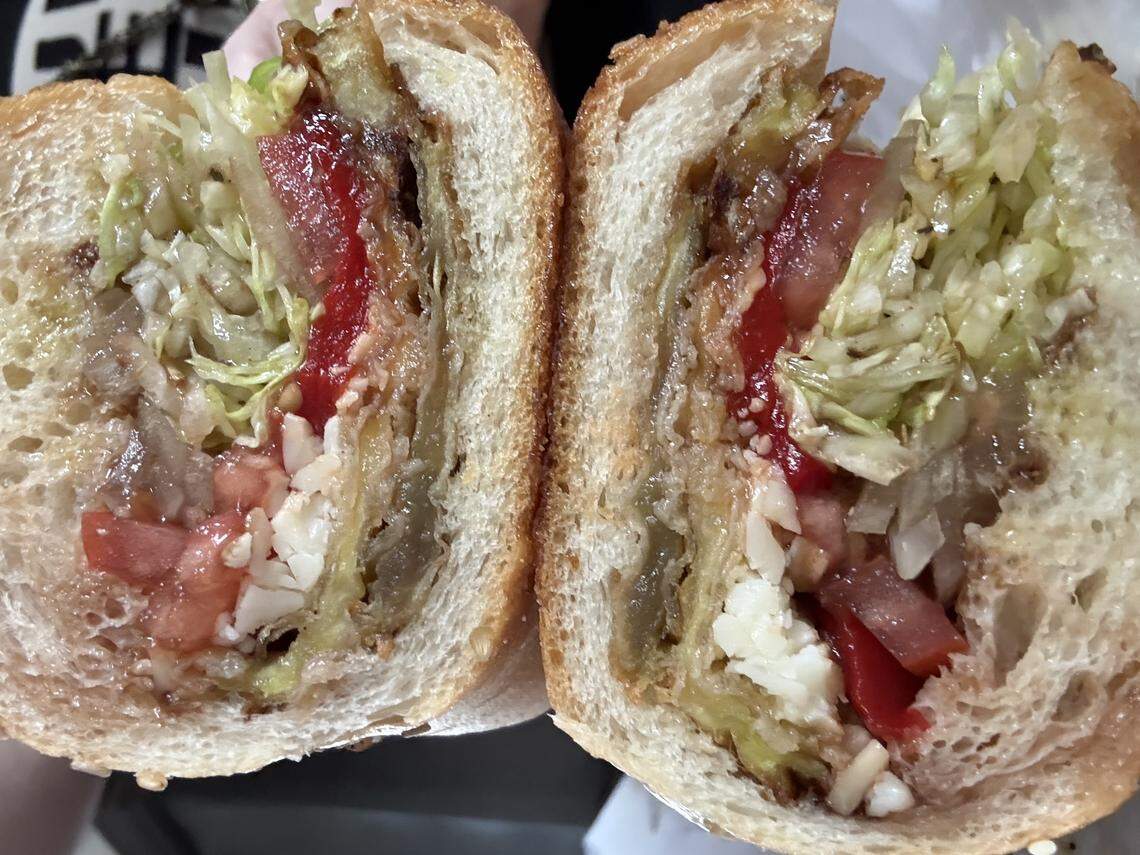 A cross-section of a hoagie on a sesame-seeded roll reveals layers of shredded lettuce, sliced tomatoes, red peppers and onions.