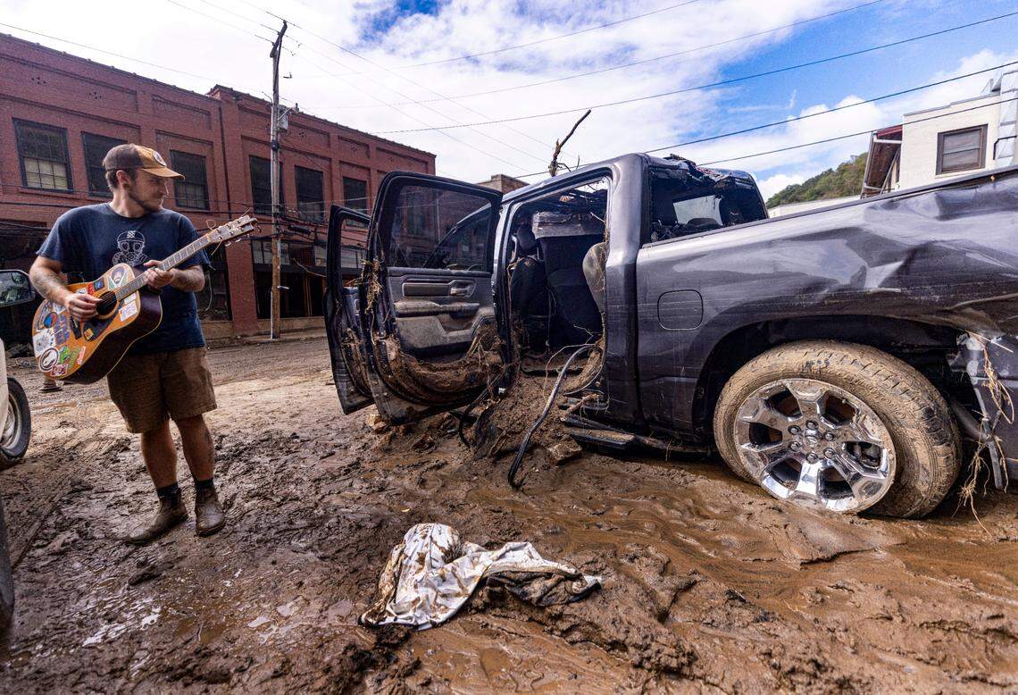 Ian Downes strums his guitar while taking a brief break from cleaning up in downtown Marshall on Tuesday, Oct. 1, 2024 after the French Broad River caused catastrophic flooding. The remnants of Hurricane Helene caused widespread flooding, downed trees, and power outages in western North Carolina.