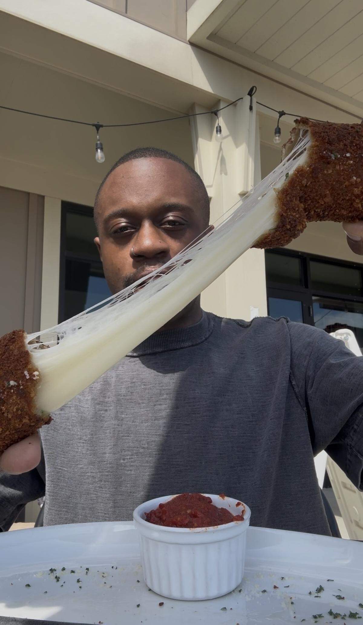 A person pulling apart a massive, deep-fried mozzarella stick to reveal a long, thick string of melted cheese.