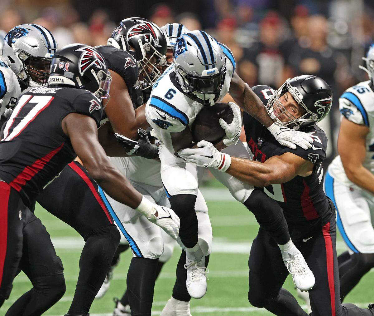 Carolina Panthers running back Miles Sanders, center, leaps through a hole in the Atlanta Falcons defense on a run during first-quarter action at Mercedes-Benz Stadium in Atlanta, GA on Sunday, September 10, 2023.