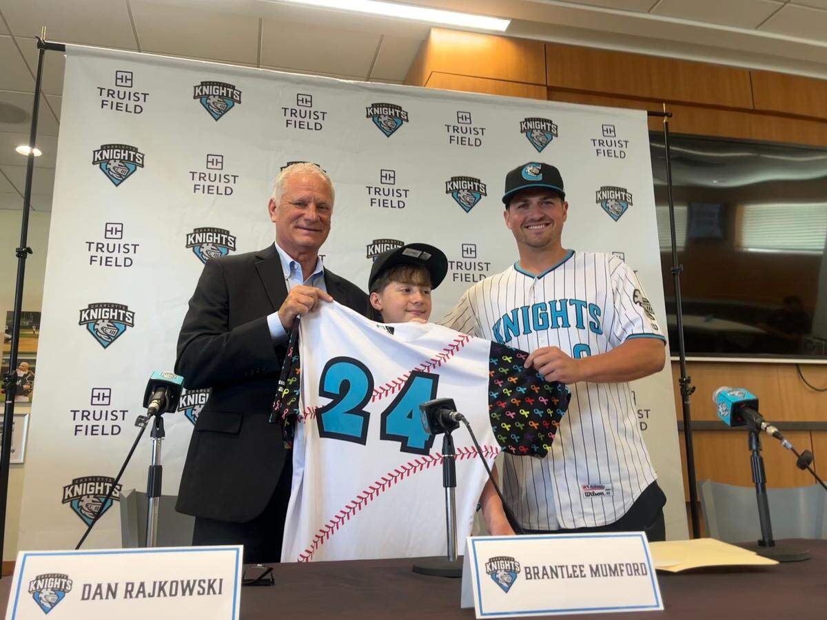 Charlotte Knights COO Dan Rajkowski, left, and manager Justin Jirschele, right, pose with Brantlee Mumford after signing the 11-year-old to a one-day contract.