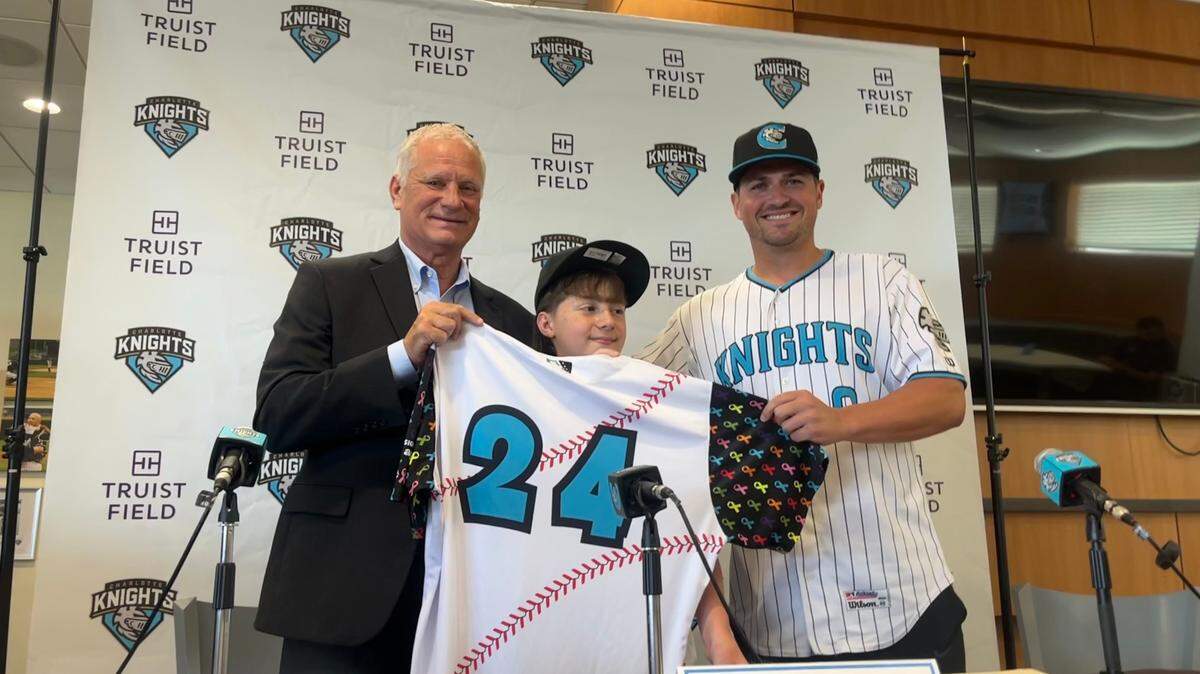 Charlotte Knights COO Dan Rajkowski, left, and manager Justin Jirschele, right, pose with Brantlee Mumford after signing the 11-year-old to a one-day contract.